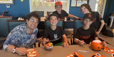 Kids and an elderly woman painting Halloween pumpkins together.
