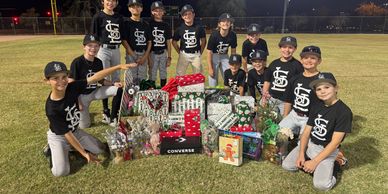 Youth baseball team with holiday gifts on field.