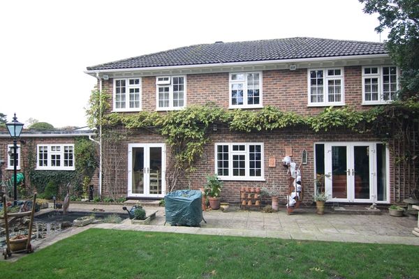 Two-story brick house with patio and garden, featuring white-framed windows and climbing plants.