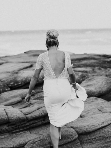 Woman in a white dress walking on rocky terrain by the ocean.