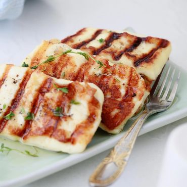 Grilled halloumi cheese garnished with herbs on a plate with a fork.