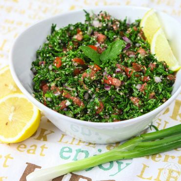 Fresh tabbouleh salad with lemon wedges and green onions.