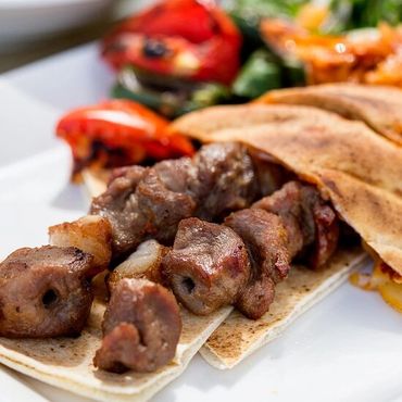 Grilled meat skewers served with flatbread and grilled vegetables.
