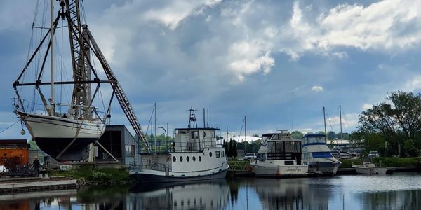 Boat lifted by crane over calm water with cloudy sky reflection.