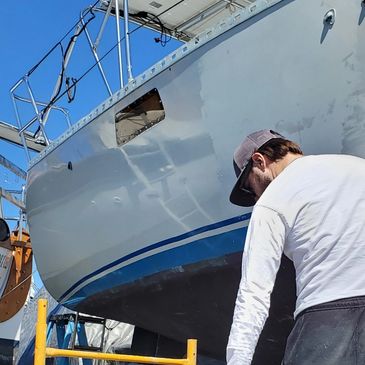 Man working on a boat hull under clear blue sky.