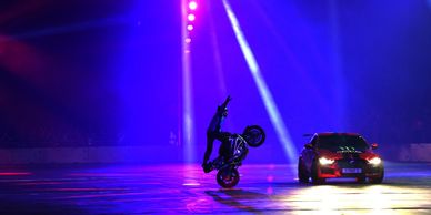 car and motorcycle perform in automotive show motorcycle rider is standing on bike while car circles