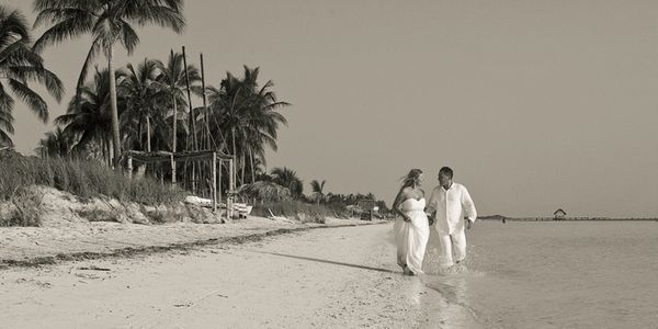 bride and groom running along the shoreline of an expansive tropical beach with palm trees