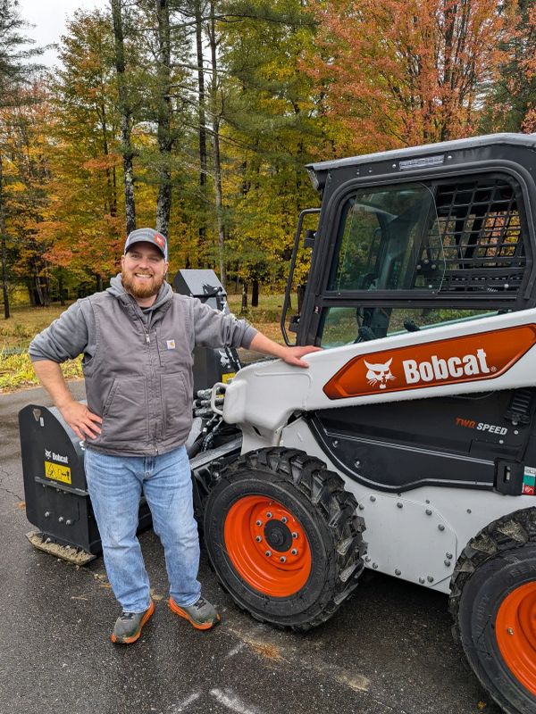 Man standing beside a Bobcat machine in autumn.