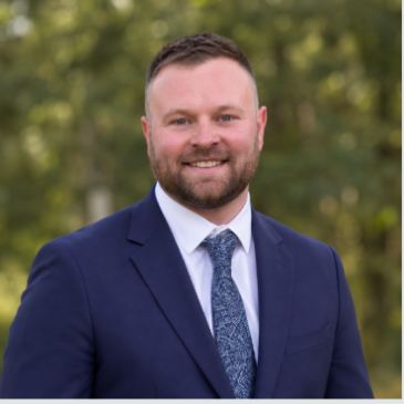Man in suit smiling outdoors.