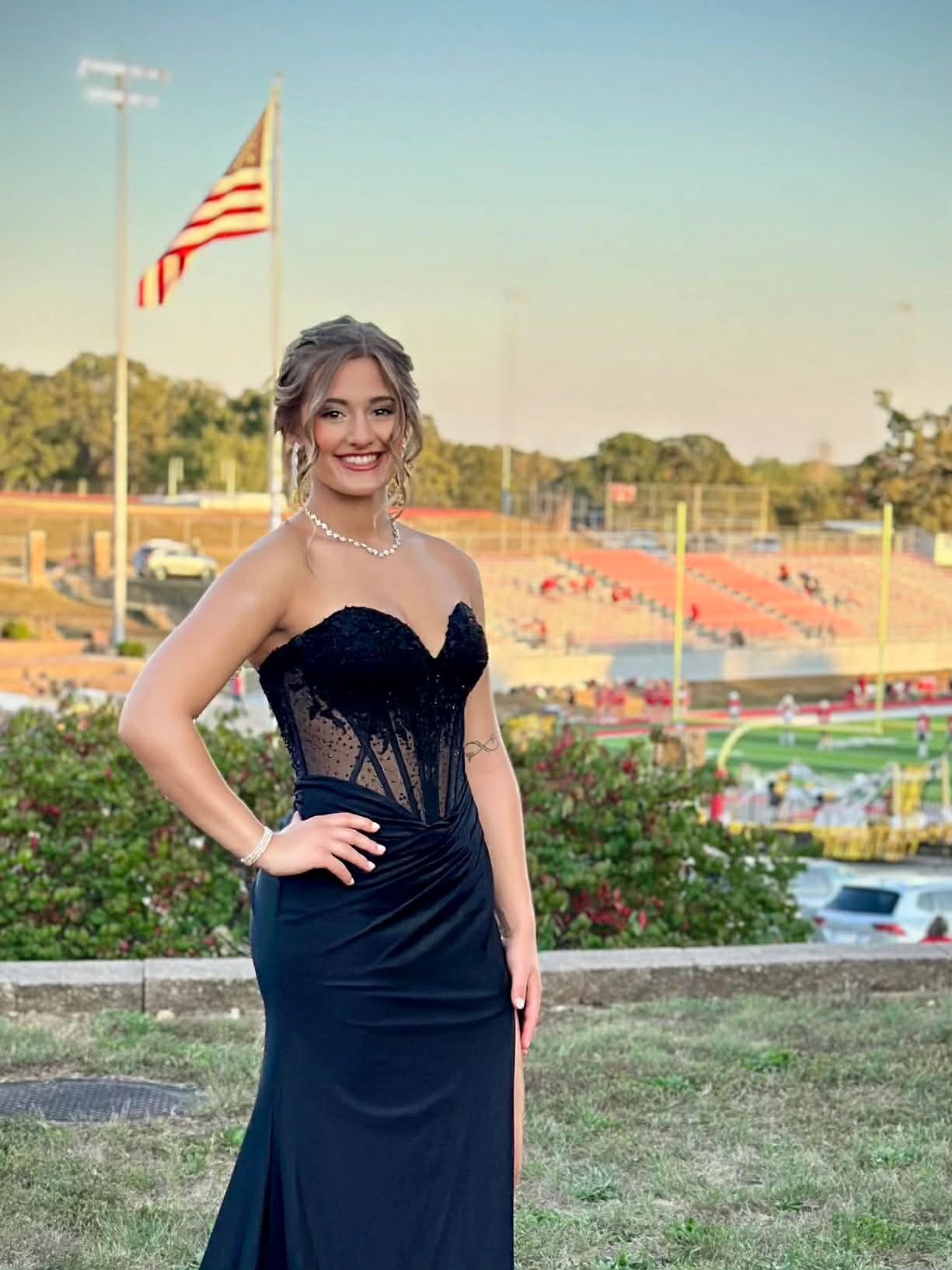 Young woman in an elegant black dress posing outdoors near a football field.