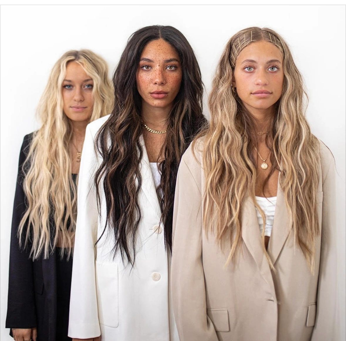 Three women with long wavy hair wearing blazers.