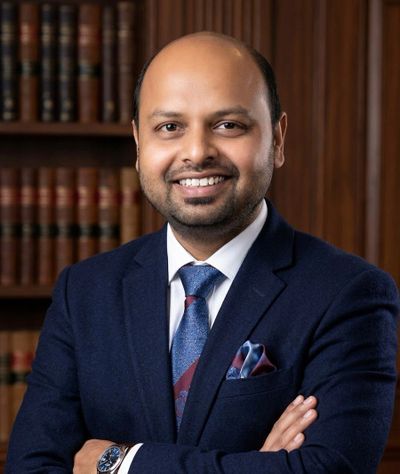 Smiling man in a suit standing with arms crossed in front of a bookshelf.