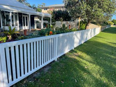 White picket fence surrounding a garden with vibrant plants and a porch.