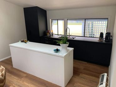 Modern kitchen with black cabinets and a white island on wood flooring.