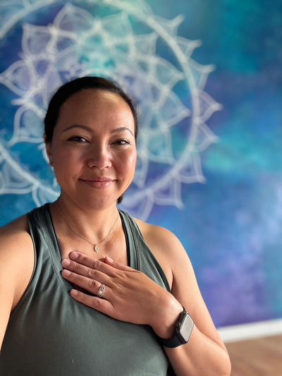 Smiling woman with hand on chest in front of a blue mandala wall art.