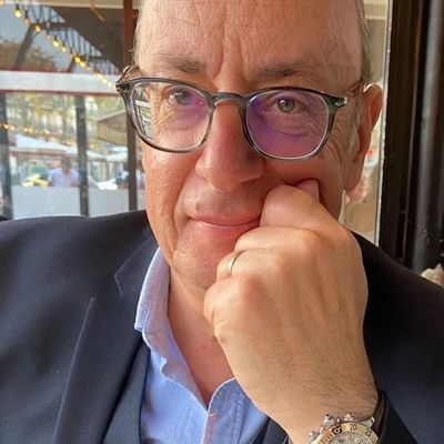 Man wearing glasses and a suit, resting his chin on his hand in a cozy café.