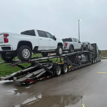 A car carrier truck loaded with multiple pickup trucks on a rainy day.