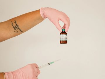 Person wearing pink gloves holding a vaccine vial and syringe.