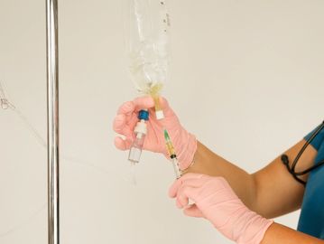 Healthcare worker preparing IV medication with pink gloves.
