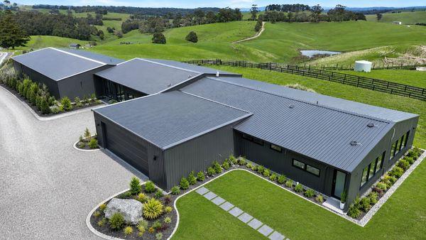 Modern black house with a large driveway in a green rural area.