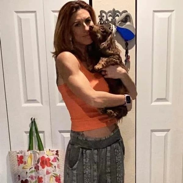Woman in orange top holding a small dog indoors.