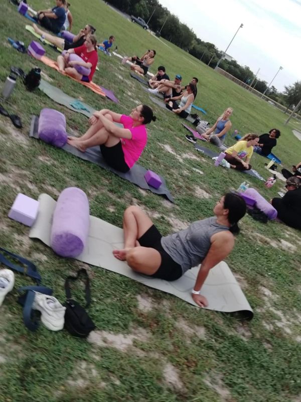 People sitting on yoga mats outdoors with purple yoga props in a grassy field.