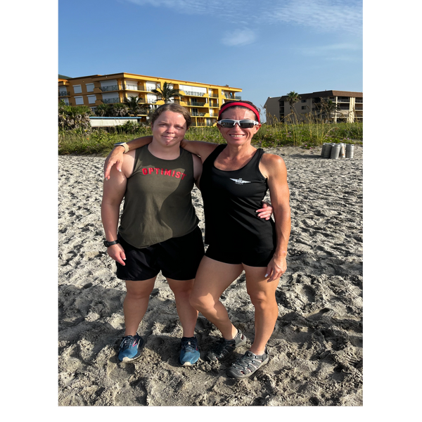 Two women in athletic wear posing together on a sunny beach.