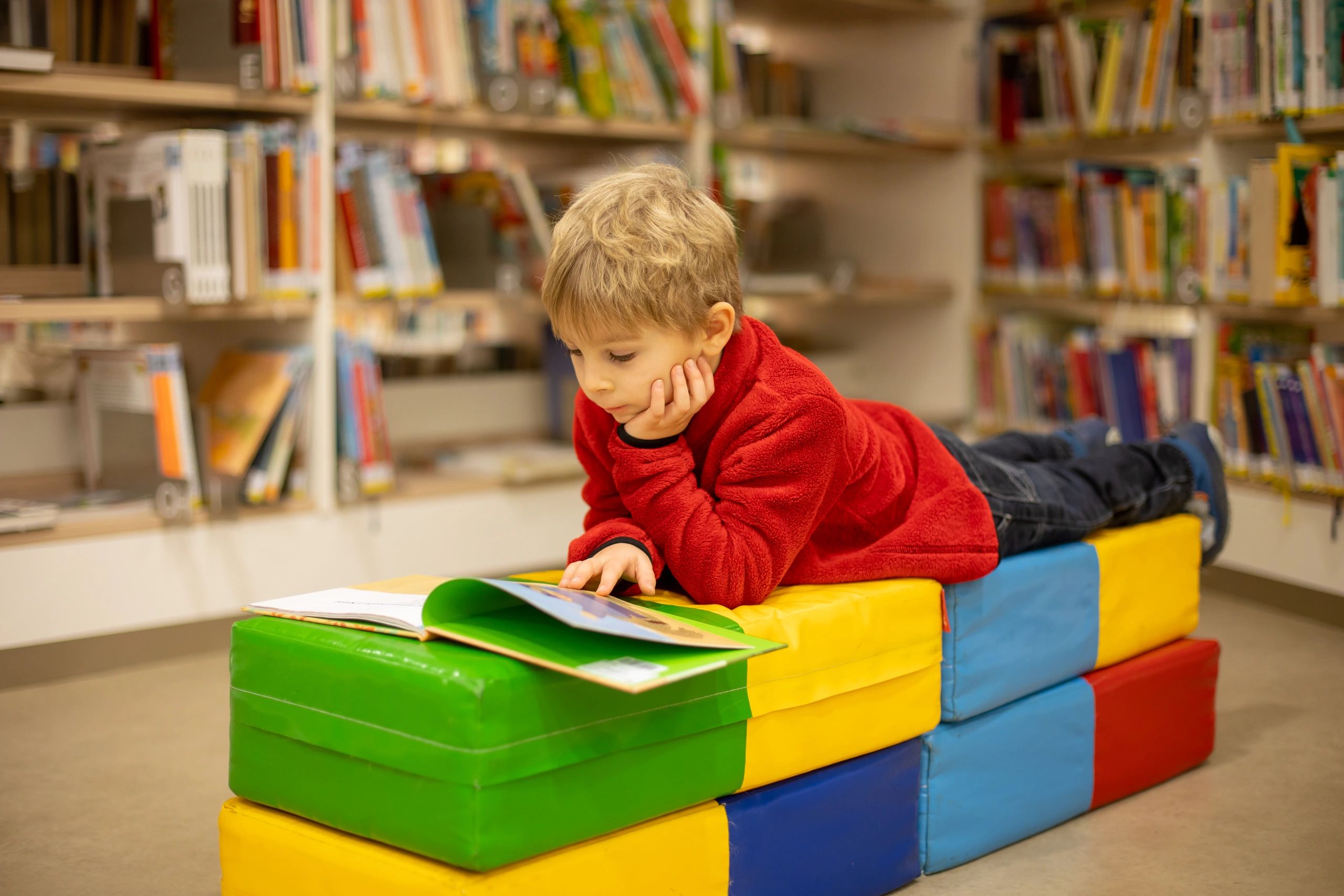 A boy holds a book open for a delighted toddler sleeping and reading.