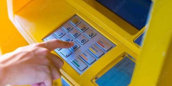 A person entering a PIN on a yellow ATM keypad.