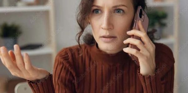Woman in brown sweater looks confused while talking on phone.