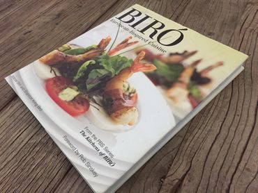 Cookbook titled "BIRÓ" featuring European-inspired cuisine with shrimp and fresh salad on cover.