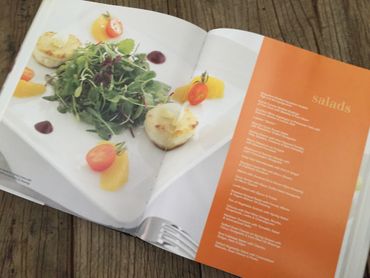 Open cookbook showing a fresh salad with tomatoes and greens on one page, salad recipes on the other.