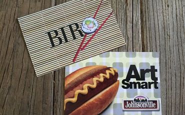 Two promotional cards on a wooden surface: one for BTR with sushi graphic, one for Johnsonville hot dogs.