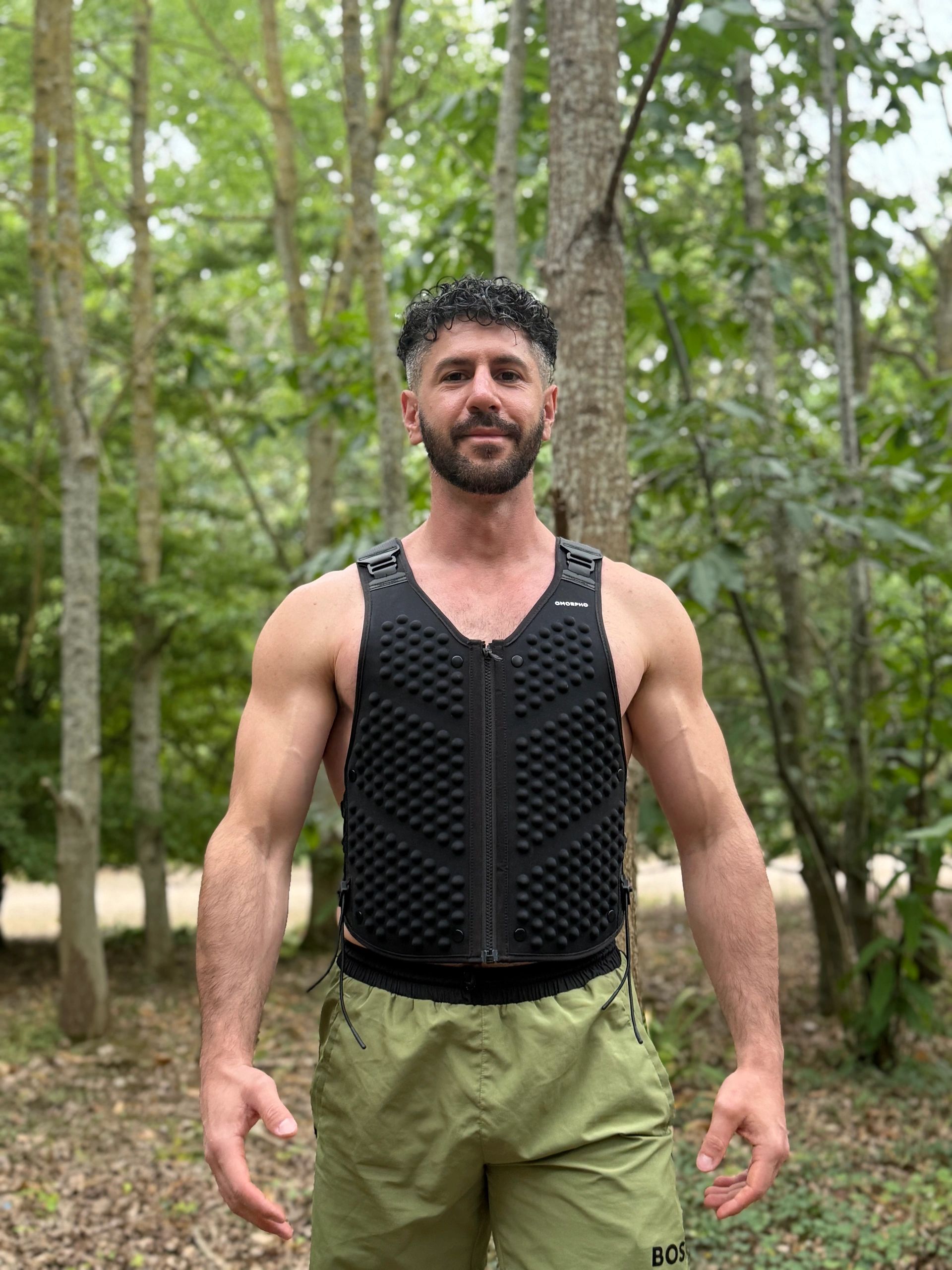 Man in a black vest standing in a forest.