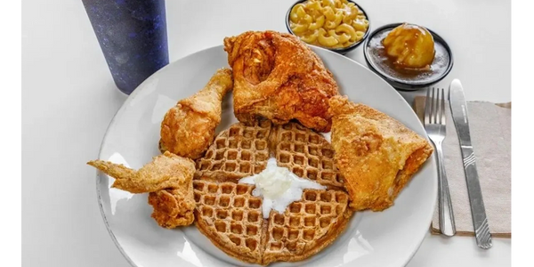A plate of fried chicken with waffles, macaroni, mashed potatoes, and a drink.