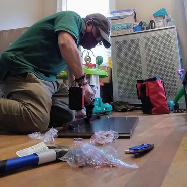 Man assembling furniture on wooden floor with tools scattered around.
