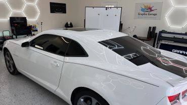 White sports car in a well-lit garage with hexagonal ceiling lights.