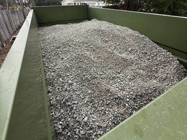 A green truck bed filled with gravel or crushed stone outdoors.