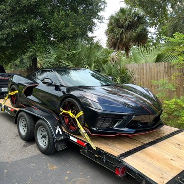 Black sports car secured on trailer hitched to a black GMC truck.