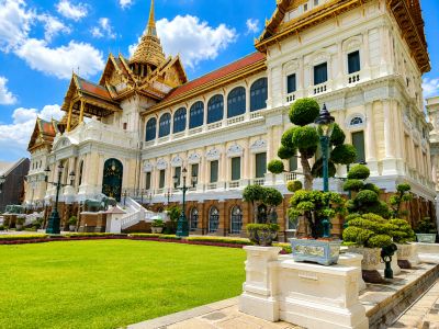 Grand palace with golden spires and manicured garden under a blue sky.