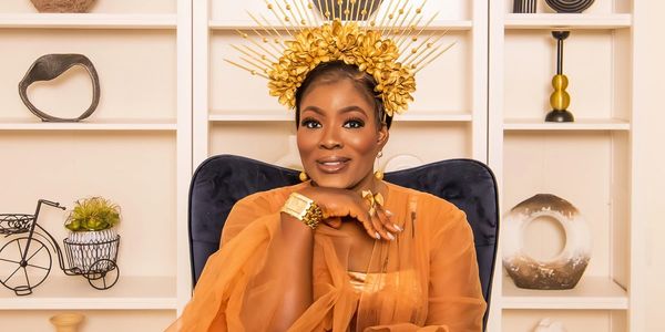 Elegant woman wearing a golden floral headpiece and orange sheer outfit sits confidently.