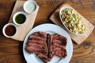Sliced medium-rare steak with macaroni and cheese and three dipping sauces.