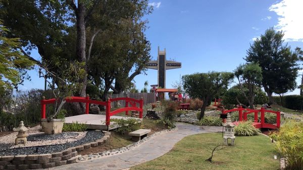 A serene garden with red wooden bridges and a tall observation tower under a clear blue sky.