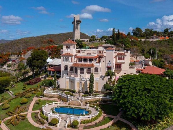 A grand villa with a pool and manicured gardens under a clear blue sky.