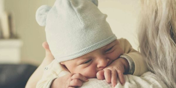 Newborn baby resting on a caregiver's shoulder wearing a soft hat.