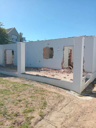 Partially demolished white-walled building under clear blue sky.