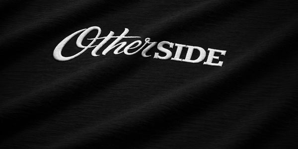 Embroidered text 'Other SIDE' on black fabric.