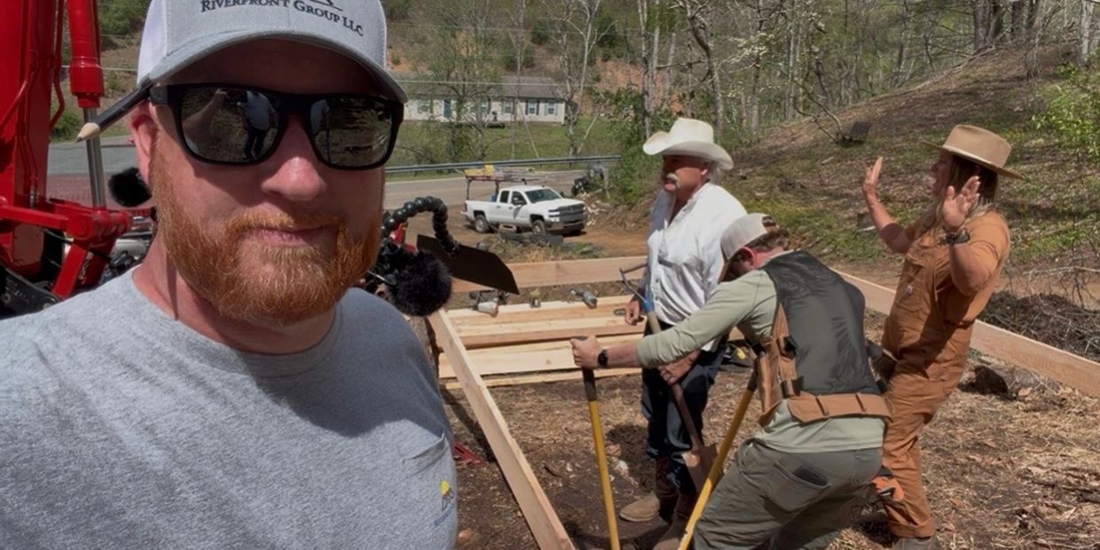 Four men working on a wooden frame outdoors in a rural area.