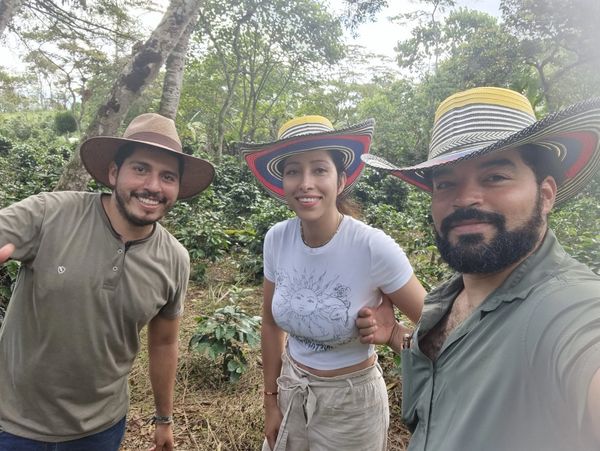 Three people in hats smiling in a lush green outdoor setting.