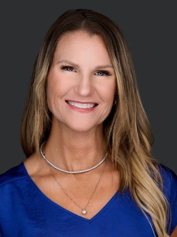Smiling woman with long hair wearing a blue top and jewelry.